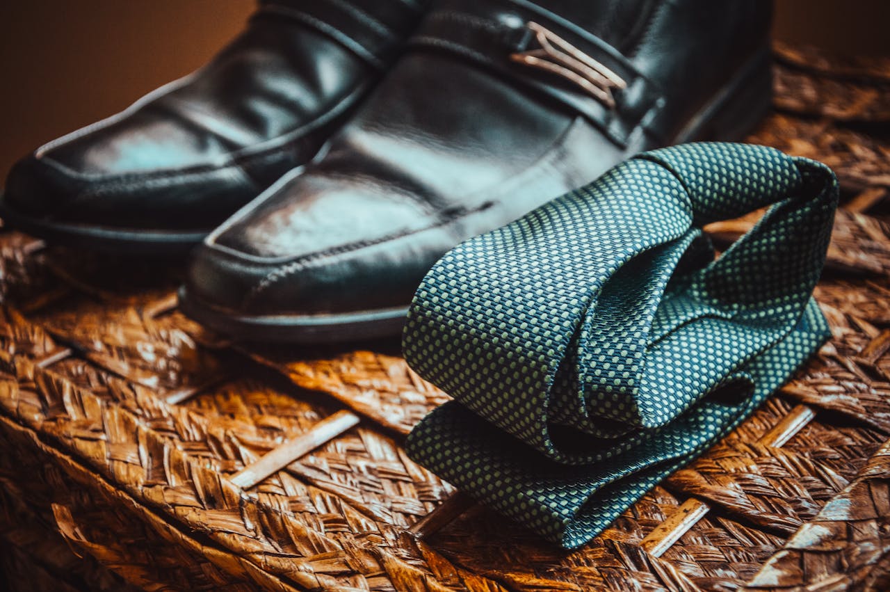 Close-up of a stylish necktie and polished leather shoes resting on a woven wicker surface.