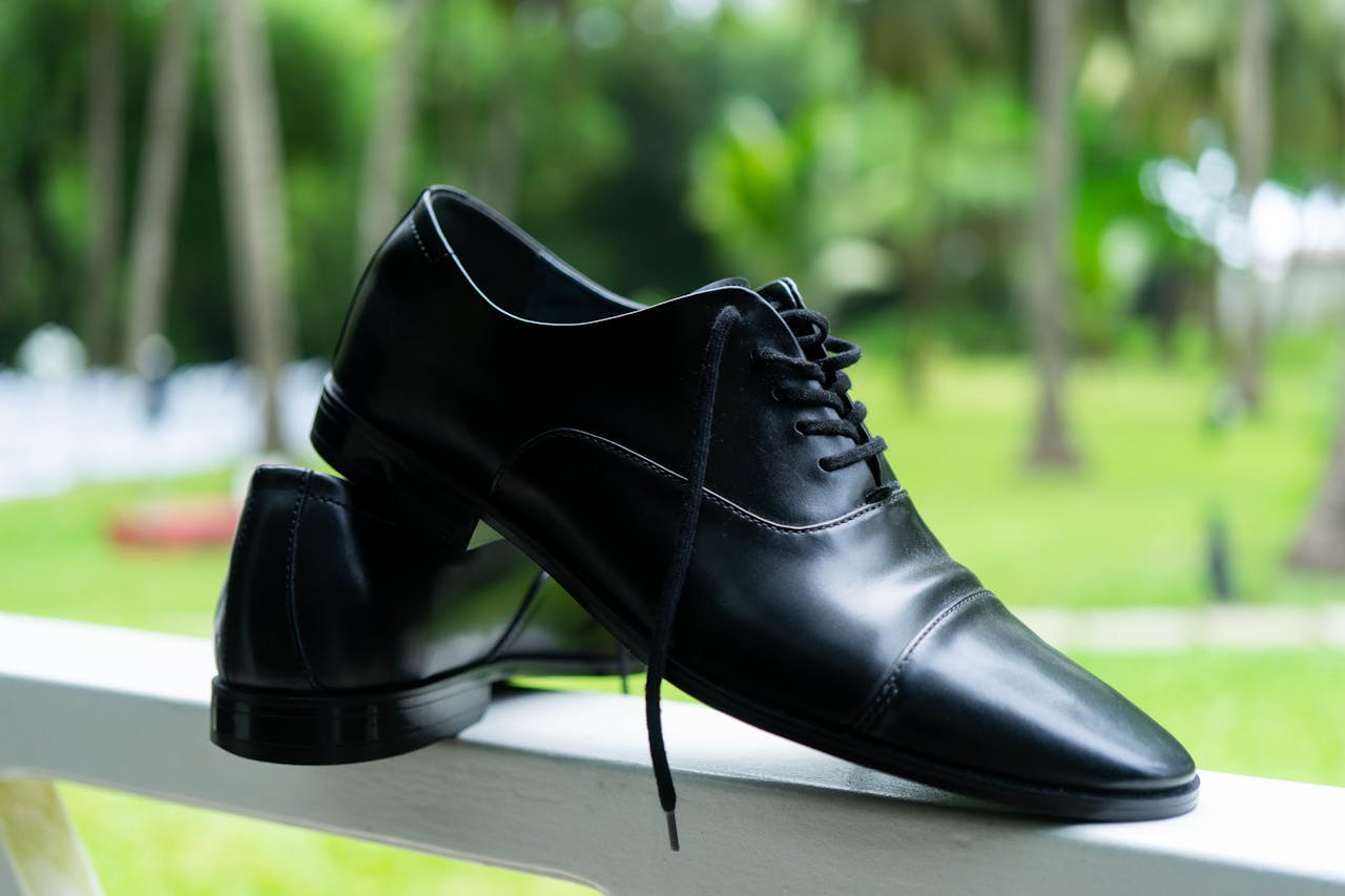 Sleek black formal shoes elegantly displayed on a handrail in a lush green outdoor setting.